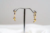 A pair of gold vermeil hoop earrings with a dolphin design dangling from the hoops, displayed against a white background.