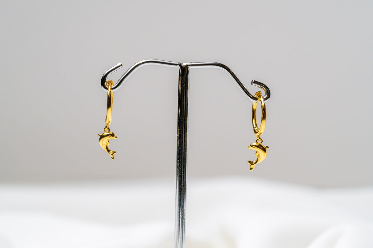 A pair of gold vermeil hoop earrings with a dolphin design dangling from the hoops, displayed against a white background.