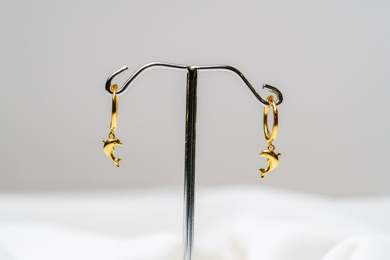 A pair of gold vermeil hoop earrings with a dolphin design dangling from the hoops, displayed against a white background.