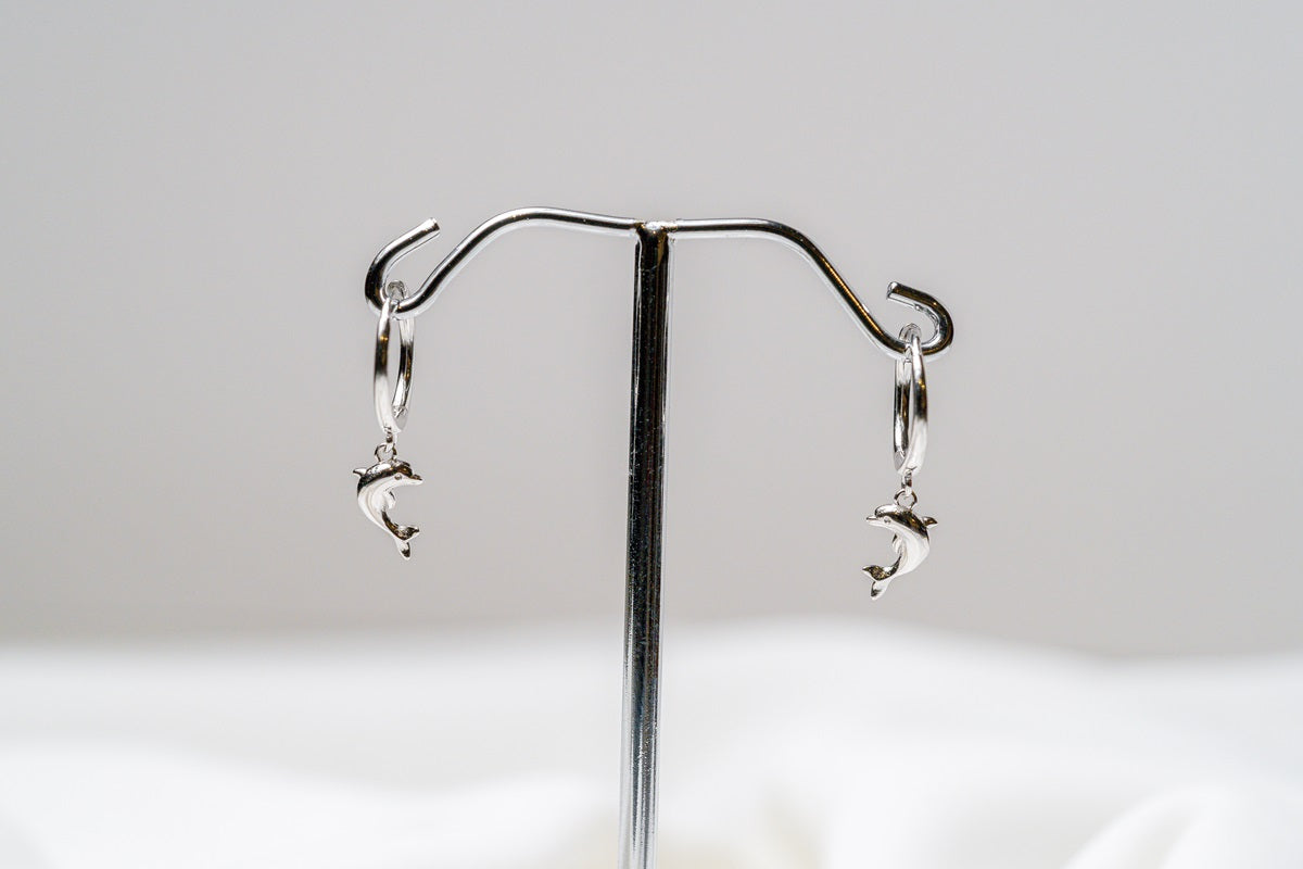 A pair of Silver hoop earrings with a dolphin design dangling from the hoops, displayed against a white background.