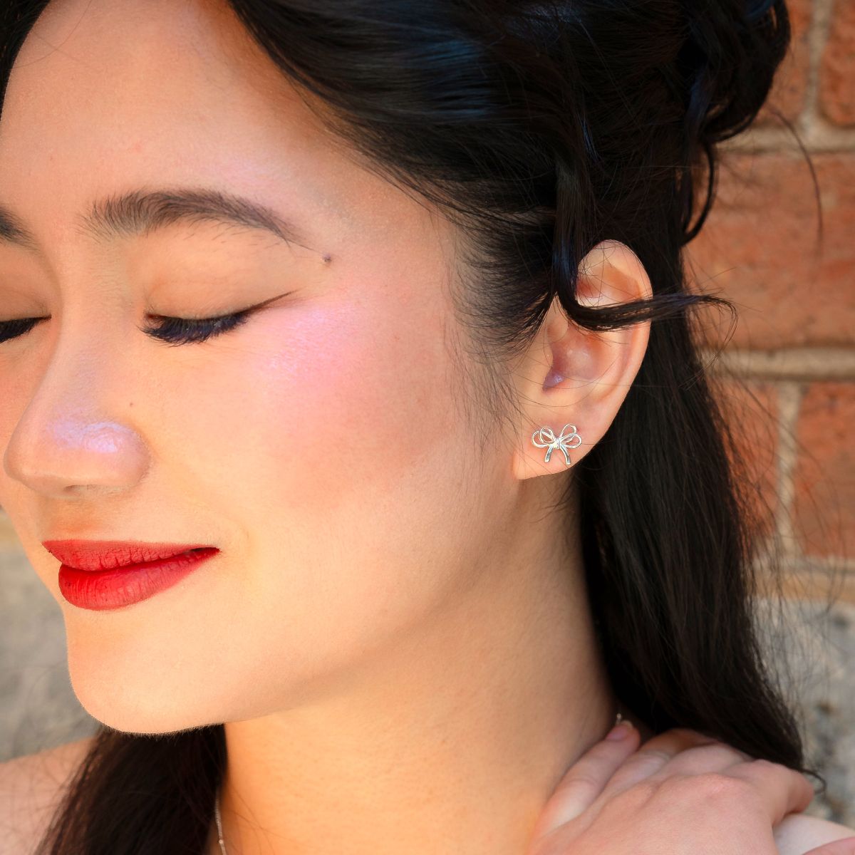Close-up of a woman wearing a silver earring with a bow or ribbon earrings design
