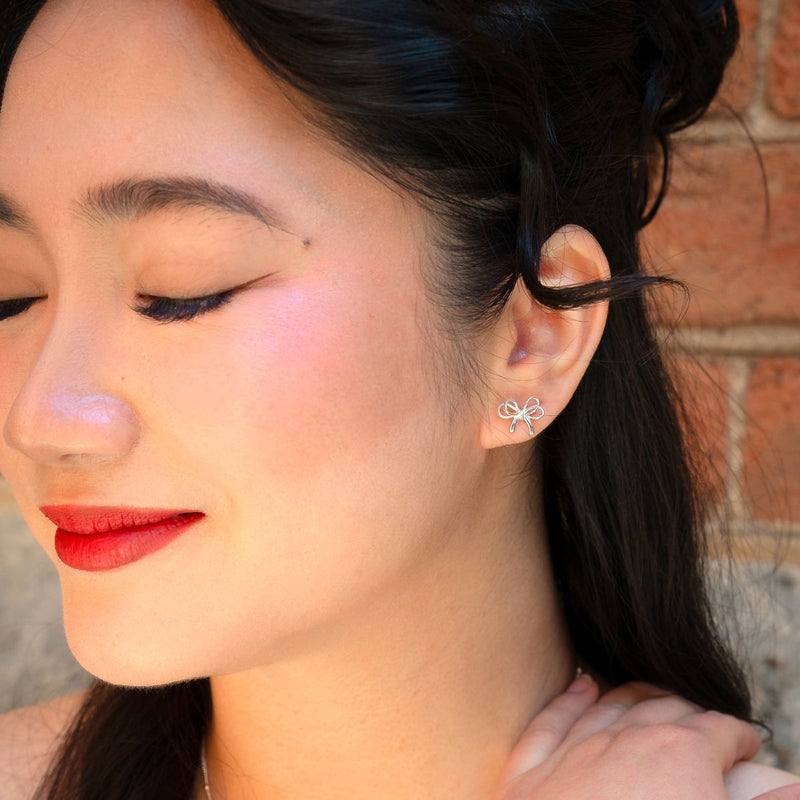 Close-up of a woman wearing a silver earring with a bow or ribbon earrings design