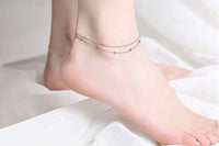 A close up of a foot wearing a double layered silver anklet.