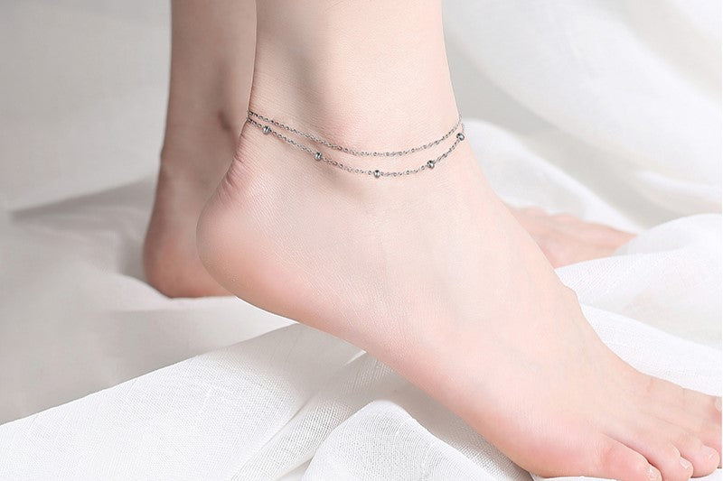 A close up of a foot wearing a double layered silver anklet.