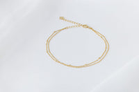 A gold-colored double-layered anklet, displayed on a white background.