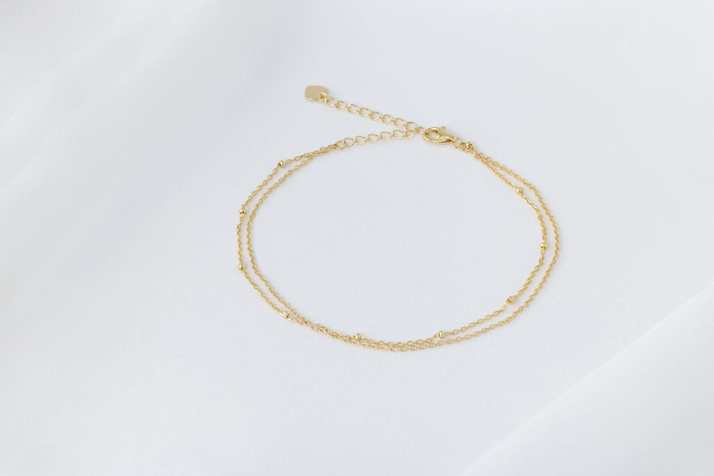 A gold-colored double-layered anklet, displayed on a white background.