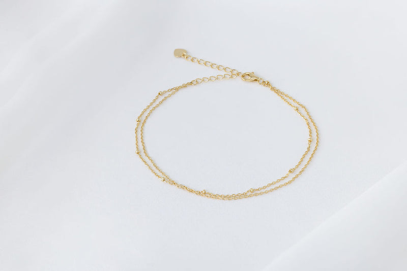 A gold-colored double-layered anklet, displayed on a white background.