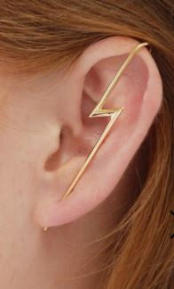 A silver ear climber earring in the shape of a lightning bolt, worn on an ear.