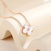 A gold necklace with a floral pendant in the center, resembling a clover leaf, on a white background.