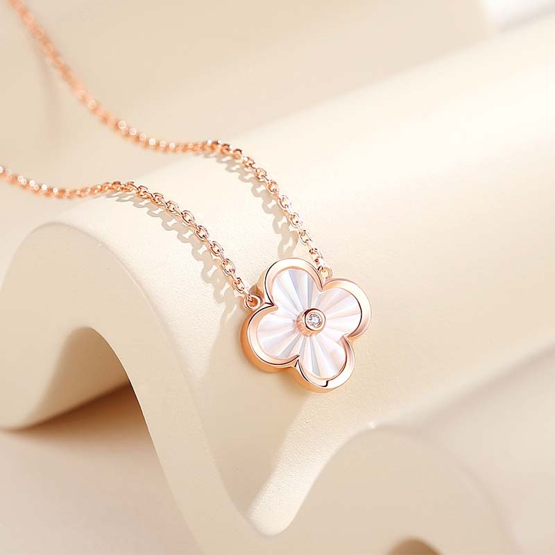 A gold necklace with a floral pendant in the center, resembling a clover leaf, on a white background.