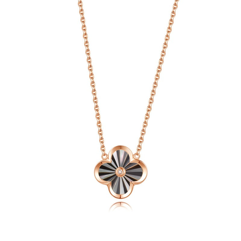 A gold necklace with a floral pendant in the center, resembling a clover leaf, on a white background.