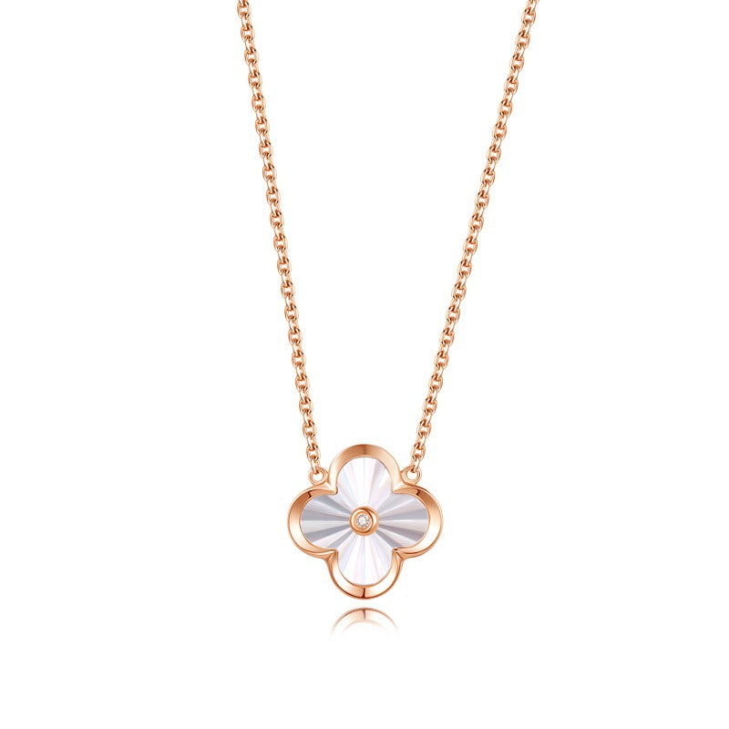 A gold necklace with a floral pendant in the center, resembling a clover leaf, on a white background.