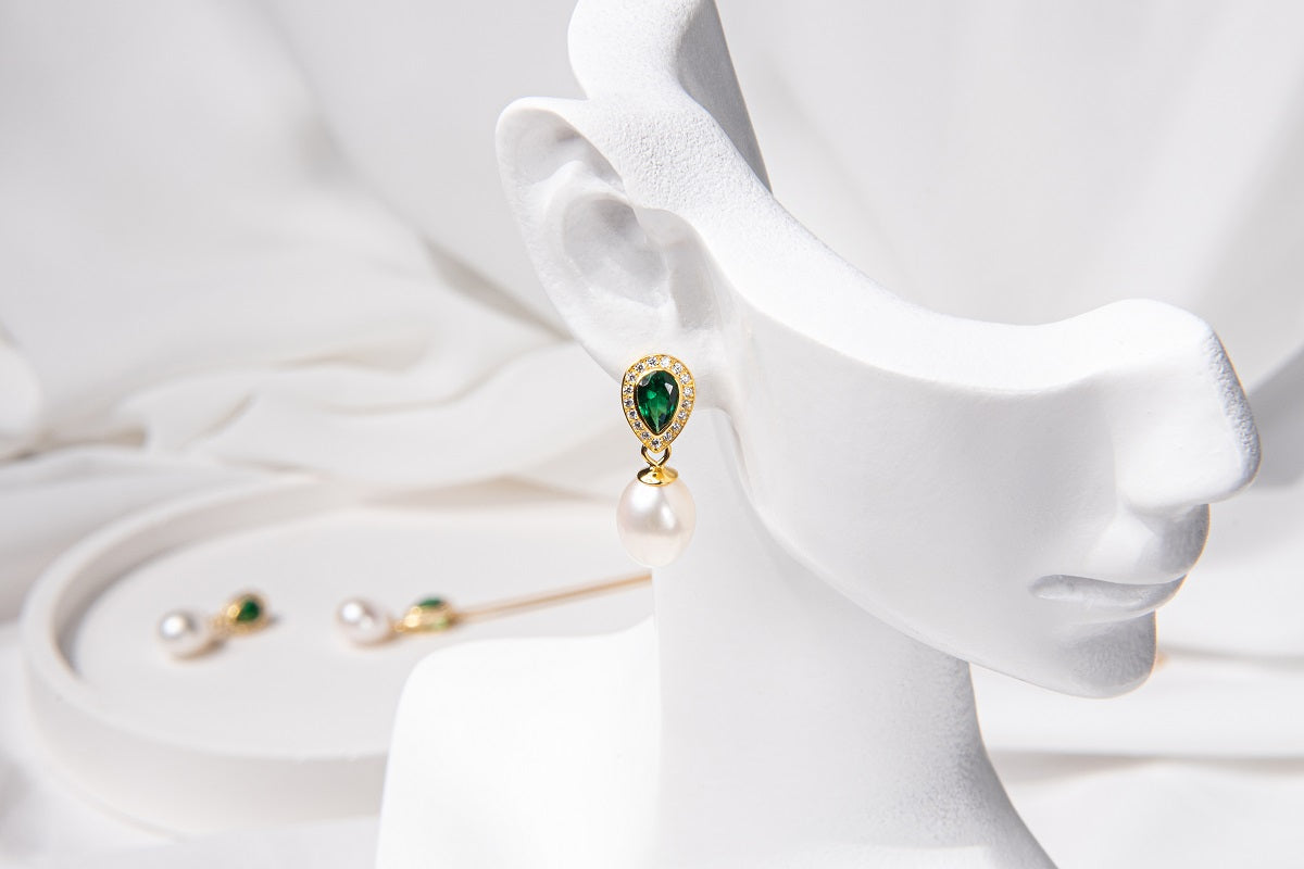 Emerald and pearl earring on a white mdel head with emerald and pearl earrings in the blurred background