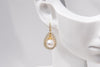 A pair of gold-colored Encanto pearl earrings displayed on a mannequin ear.