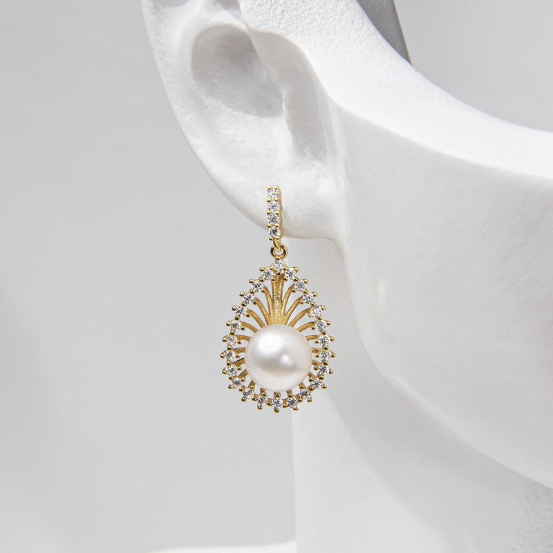 A pair of gold-colored Encanto pearl earrings displayed on a mannequin ear.
