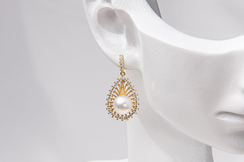 A pair of gold-colored Encanto pearl earrings displayed on a mannequin ear.