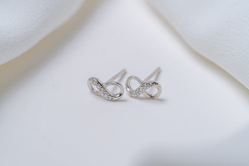 A pair of stud earrings with a butterfly back design, made of sterling silver, displayed on a white fabric surface.