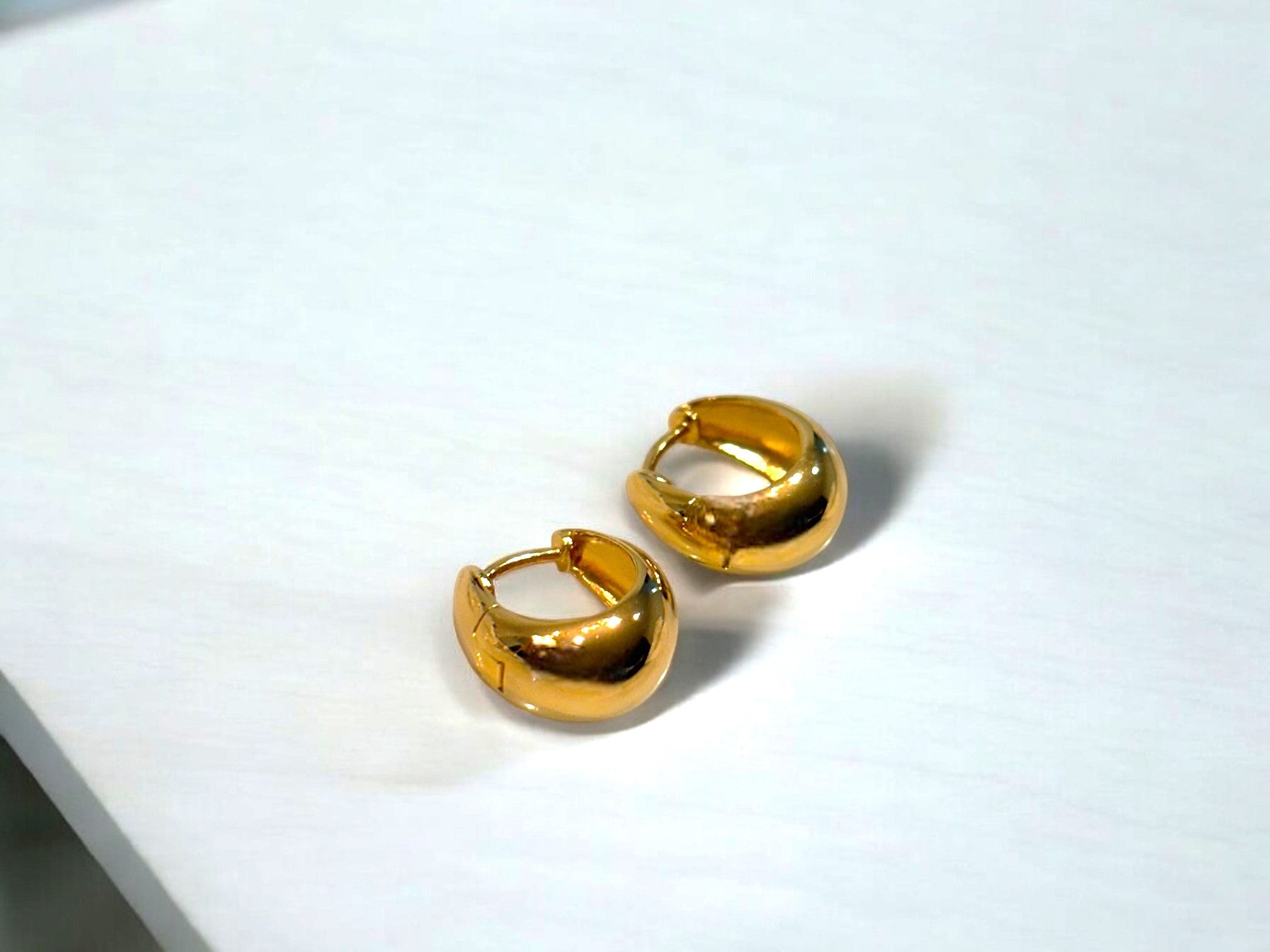 A pair of gold vermeil hoop earrings displayed on a white stone surface.