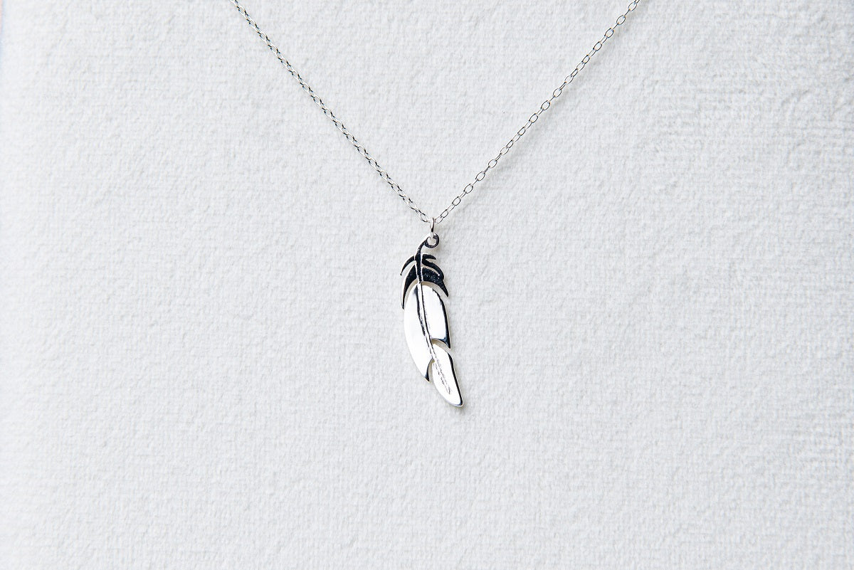 A sterling silver necklace with a pendant feather charm, displayed against a white background.
