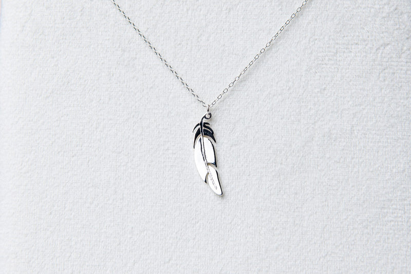 A sterling silver necklace with a pendant feather charm, displayed against a white background.