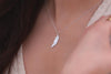A sterling silver necklace with a pendant feather charm, worn by a woman