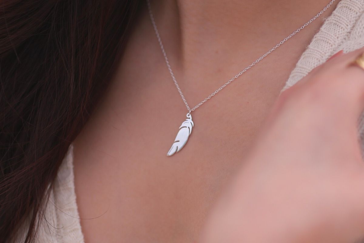 A sterling silver necklace with a pendant feather charm, worn by a woman