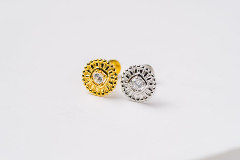 A pair of gold and silver colored earrings with a floral pattern and a central cubic zirconia on a white background.