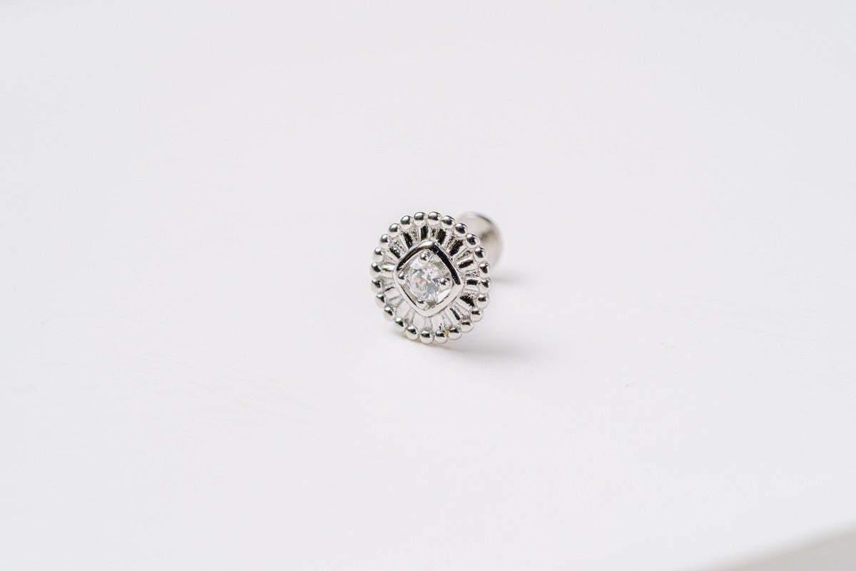 A silver colored earring with a floral pattern and a central cubic zirconia on a white background.