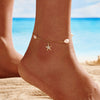 A close up of a womans foot wearing a gold and pearl anklet with a starfish pendant with a beach background