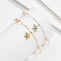 A gold and a silver anklet on a display. Featureing pearls and a starfish pendant.