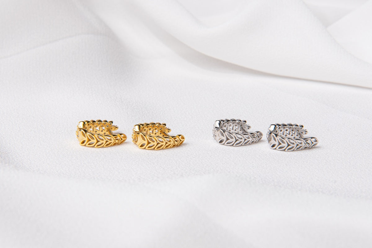 A pair of gold vermeil and sterling silver hoop earrings with leaf patterns displayed on a white fabric surface.