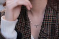 A person wearing a heartbeat necklace with a silver pendant and a sterling silver chain.