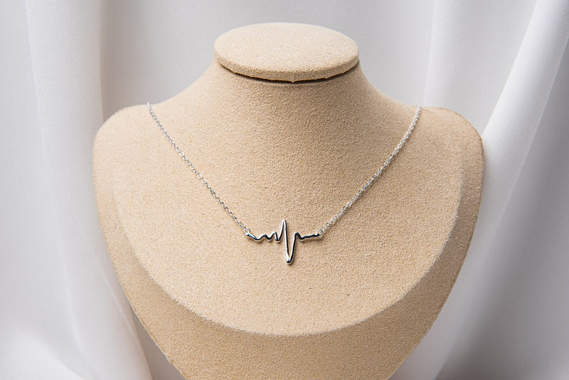 A Silver heartbeat pendant on a silver chain necklace on a bust