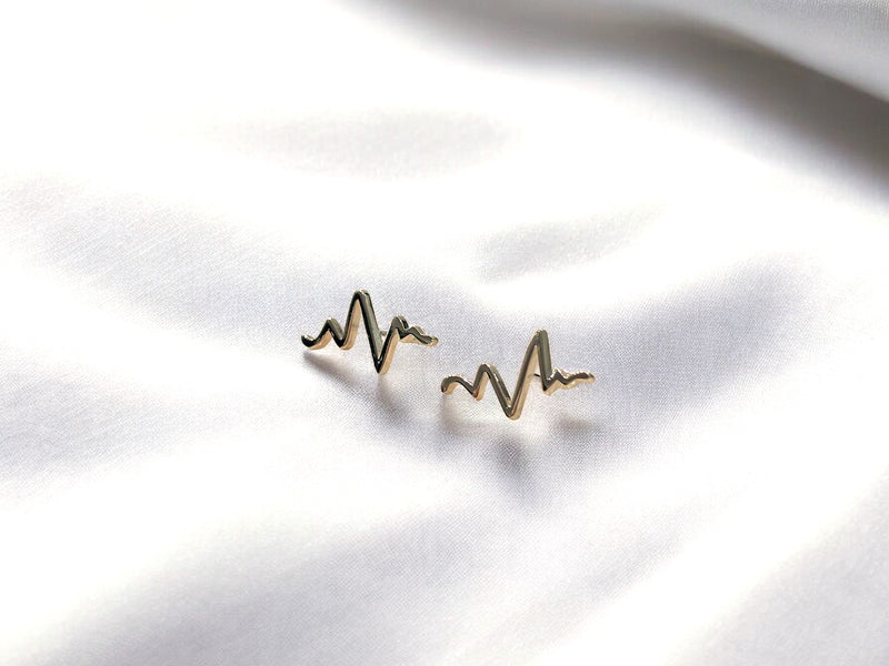 A pair of silver stud earrings with a heartbeat pattern, displayed on a white fabric background