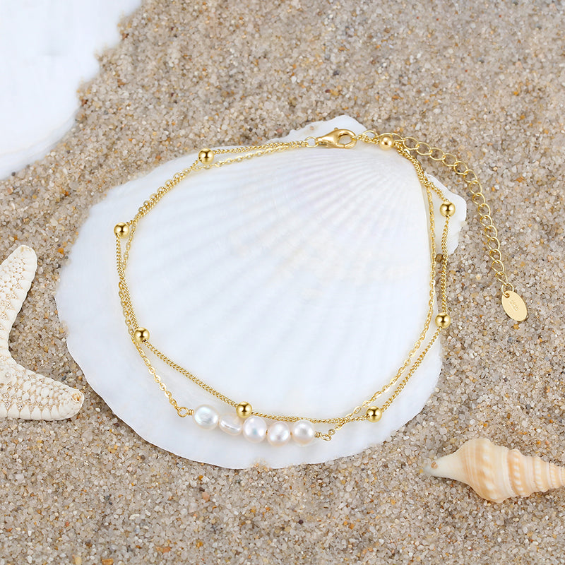 Close up of a gold anklet featuing gold balls and pearls on a beach shell