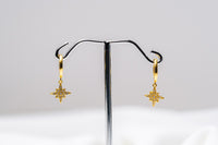 A pair of gold-colored hoop earrings with dangle diamond cubic zirconia, displayed on a silver stand against a white background.