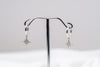 A pair of Silver hoop earrings with dangle diamond cubic zirconia, displayed on a silver stand against a white background.