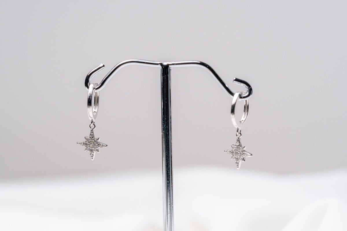 A pair of Silver hoop earrings with dangle diamond cubic zirconia, displayed on a silver stand against a white background.