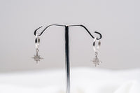 A pair of Silver hoop earrings with dangle diamond cubic zirconia, displayed on a silver stand against a white background.
