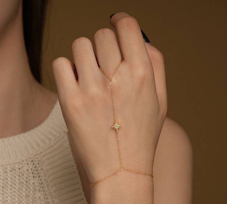 A gold vermeil bracelet with a connected ring featuring a northern star pendant, worn on a person's hand.