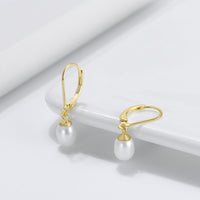 A pair of leverback pearl earrings with a  gold vermeil coating on a white background.