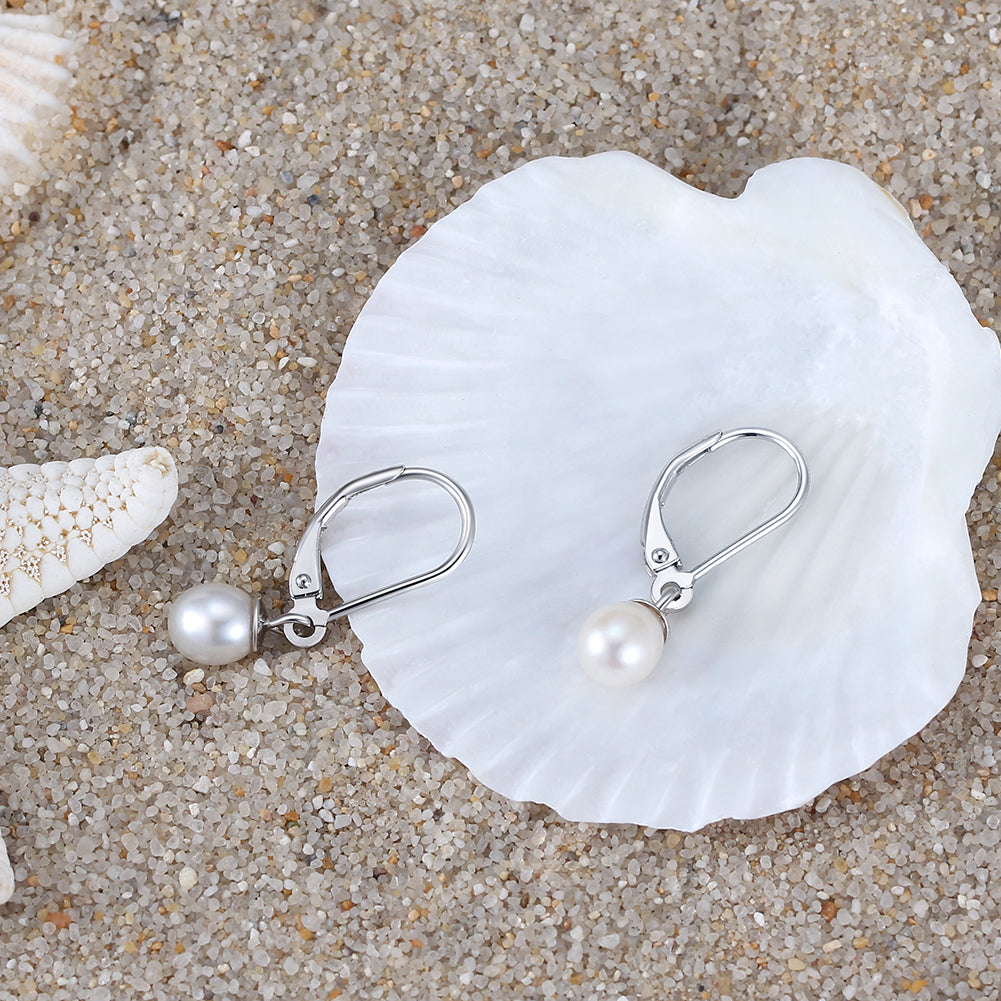A pair of silver leverback pearl earrings on a white seashell and sandy background