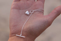 A sterling silver necklace with a small heart pendant, held in a person's hand.