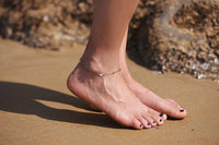Woman wearing a silver anklet featuring a heart shaped charm