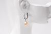 A silver earring with a champagne pearl displayed on a white mannequin head