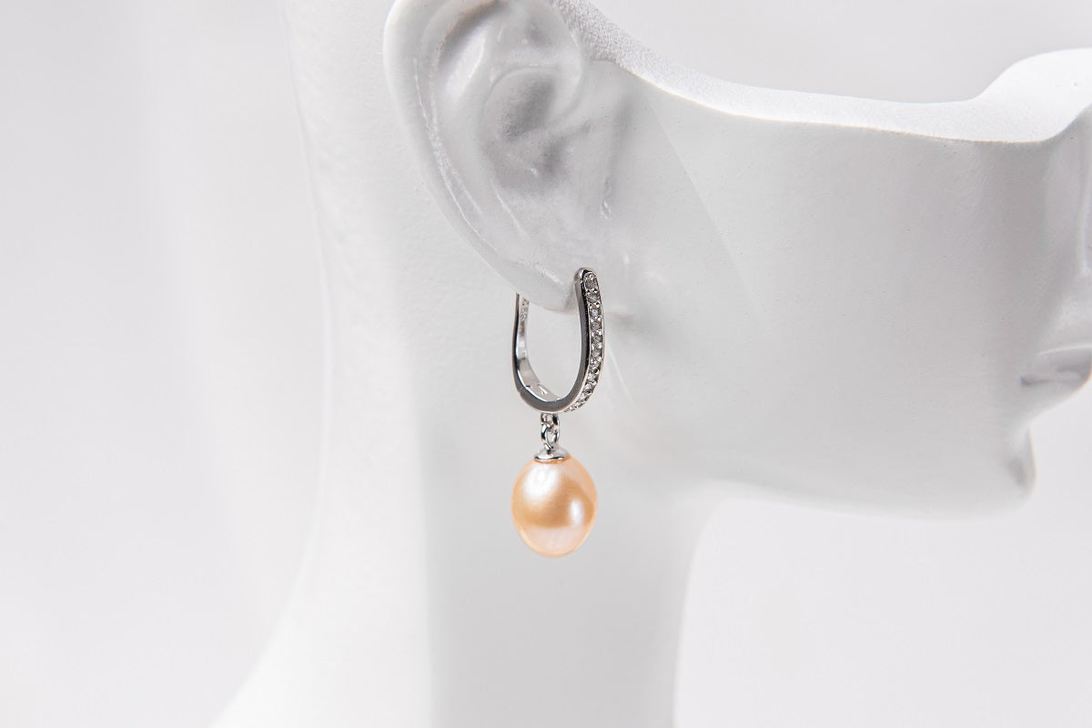 A silver earring with a champagne pearl displayed on a white mannequin head