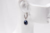 A silver earring featureing cubic zirconias and a dark blue pearl displayed on a white mannequin head
