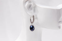 A silver earring featureing cubic zirconias and a dark blue pearl displayed on a white mannequin head