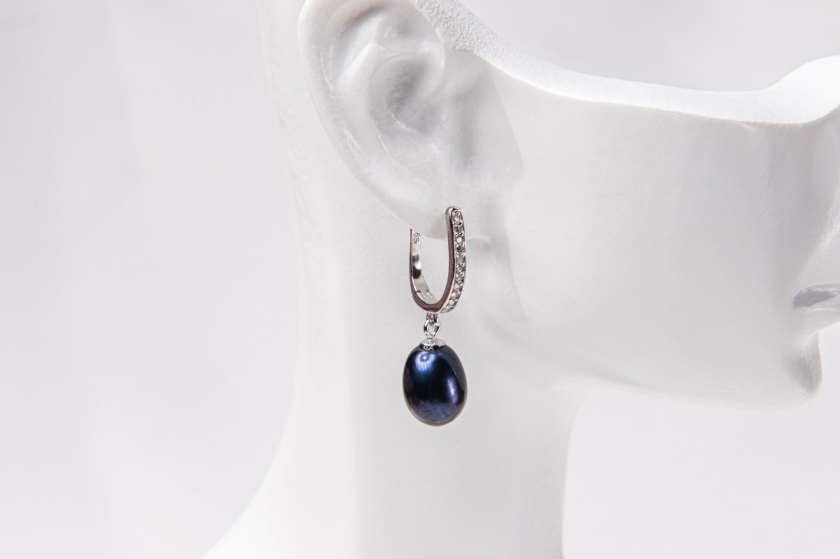 A silver earring featureing cubic zirconias and a dark blue pearl displayed on a white mannequin head