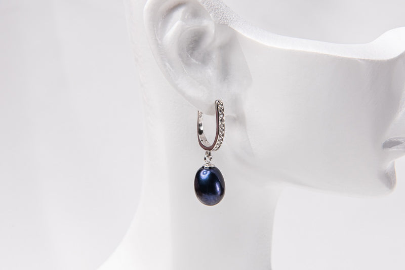 A silver earring featureing cubic zirconias and a dark blue pearl displayed on a white mannequin head